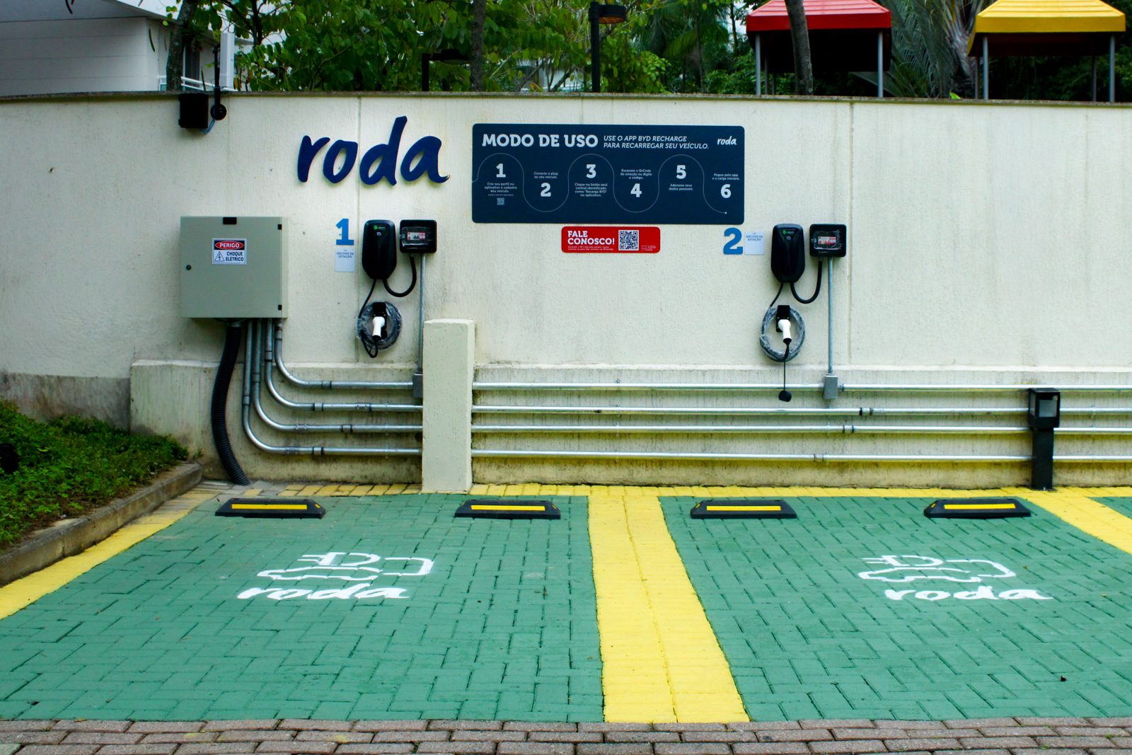 Duas vagas de recarga da Roda com carregadores de parede, placa com o modo de uso e piso sinalizado, em um condomínio atendido pela Roda Conveniência