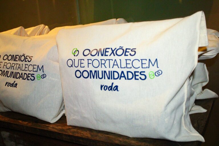 Sacolas do kit de relacionamento entregue aos síndicos, com a frase Conexões que fortalecem comunidades e a marca Roda